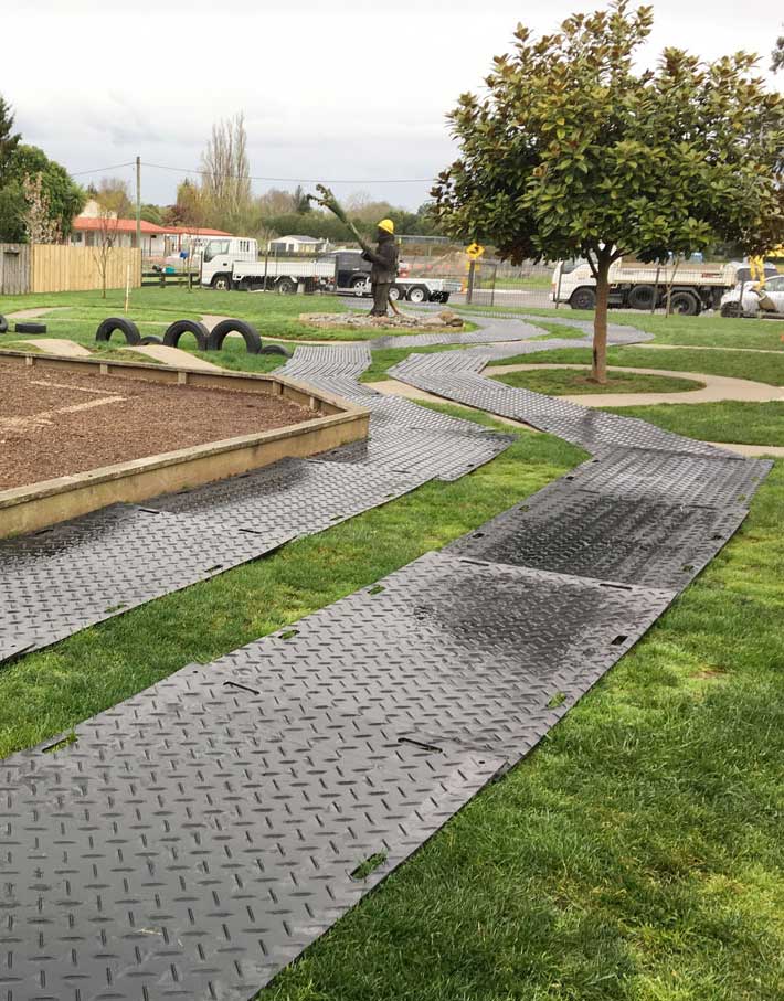 Ground protection mats laid out on grass around a playground